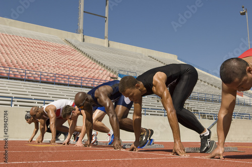 Group of multiethnic male athletes at starting blocks in racetrack