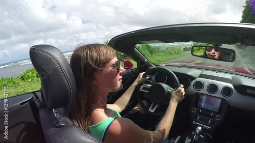 SLOW MOTION: Smiling woman driving on coastal road in luxury red convertible car photo