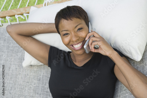 Portrait of a happy African American woman using cell phone while lying on hammock