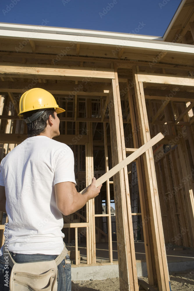 Rear view of construction worker holding wooden beam at construction site Rear view of construction worker holding wooden beam at construction site