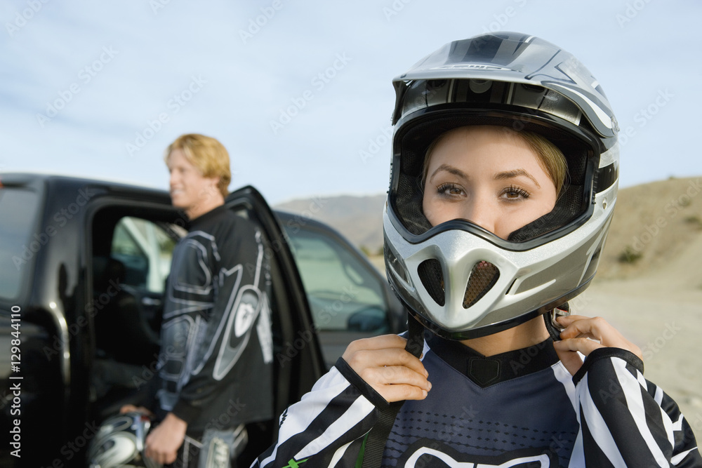 Portrait of woman wearing helmet with man and car in the background