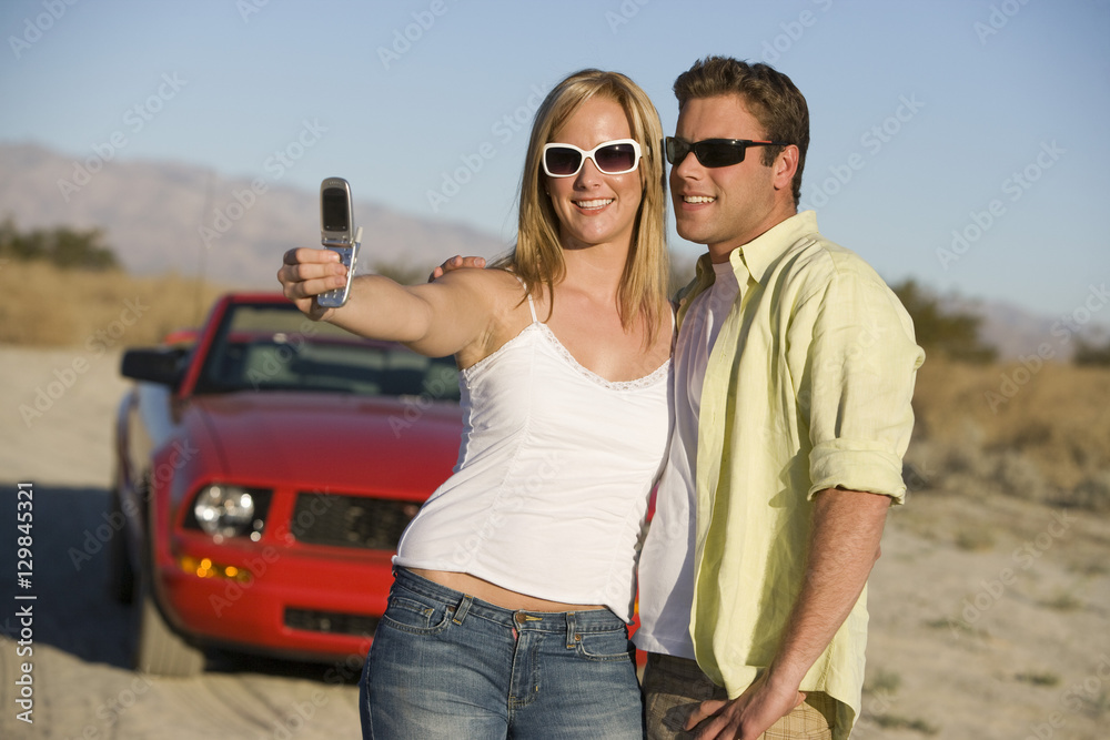 Couple taking self portrait through mobile phone with car in the background Couple taking self portrait through mobile phone with car in the background