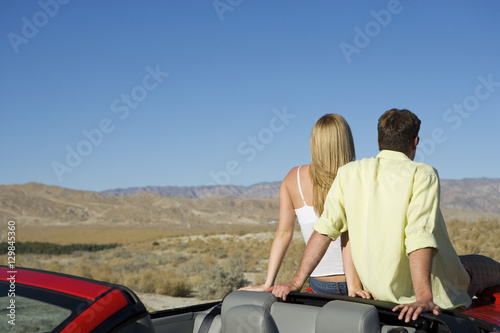 Rear view of couple sitting at backside of car looking at view