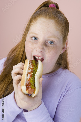 Portrait of teenage girl eating hotdog isolated over pink background