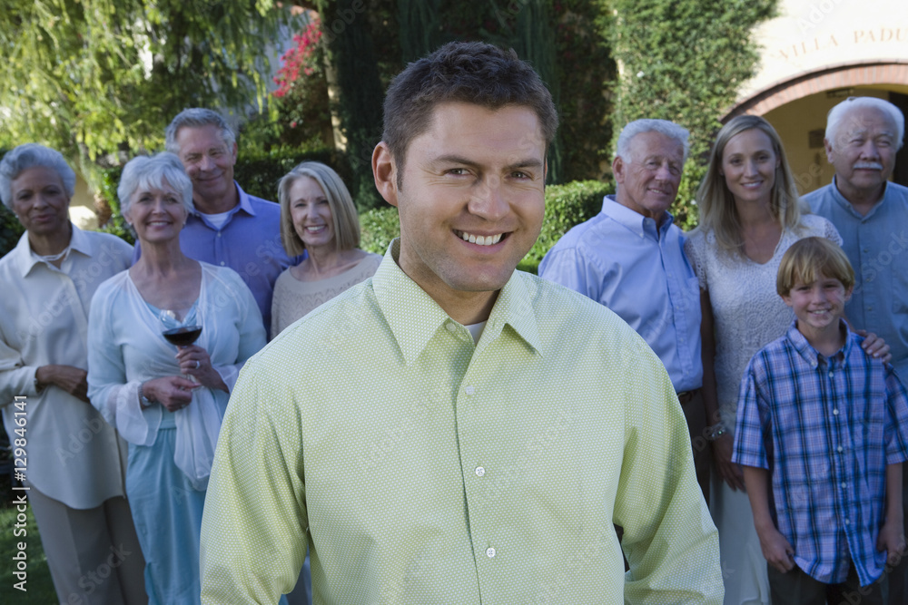 Portrait of happy middle aged man with family standing in background at lawn Portrait of happy middle aged man with family standing in background at lawn