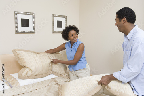 African American couple arranging pillows on their bed at home