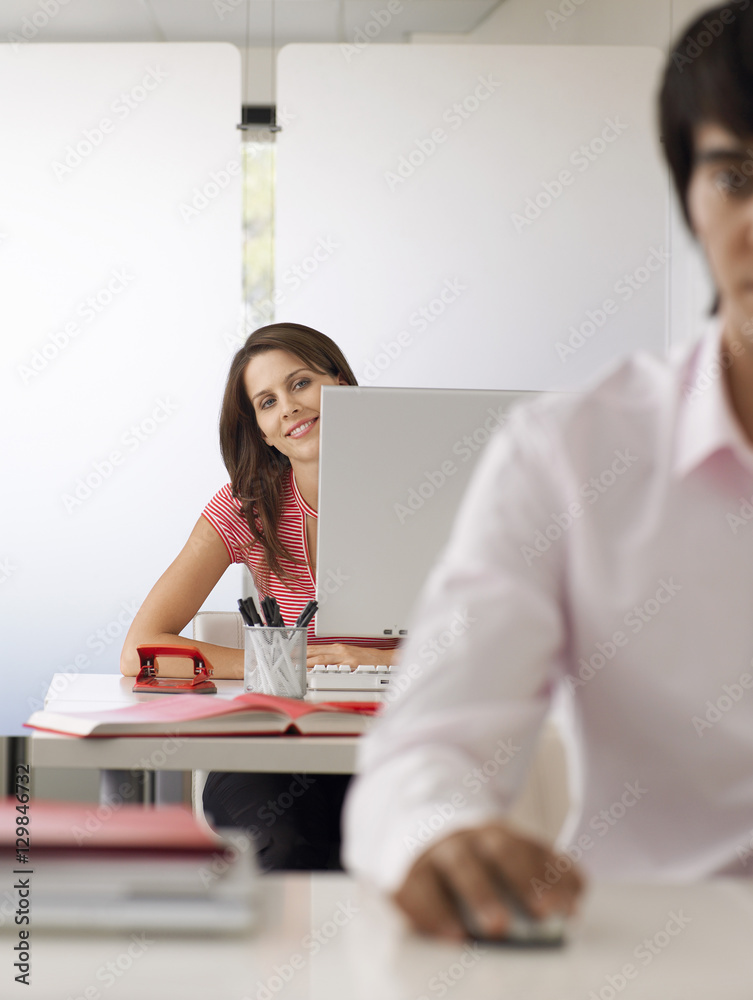 Fototapeta premium Portrait of smiling businesswoman using computer with male colleague in foreground