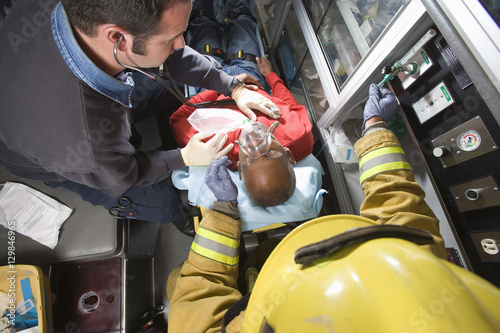 Male firefighter and EMT doctor taking care of an injured senior man in ambulance