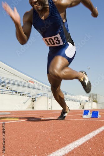 Low section of man running from starting block on track
