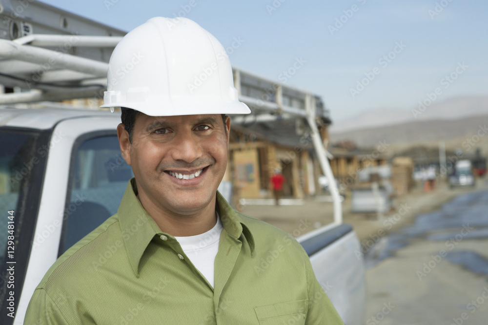 Portrait of a smiling construction worker in hardhat standing next to truck on construction site Portrait of a smiling construction worker in hardhat standing next to truck on construction site