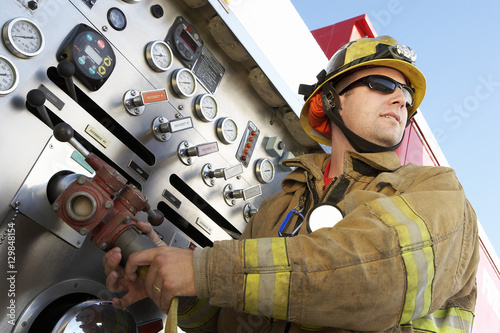 Slika na platnu Low angle view of a middle aged fire fighter holding hose