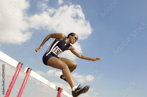 Low angle view of a female athlete jumping hurdle