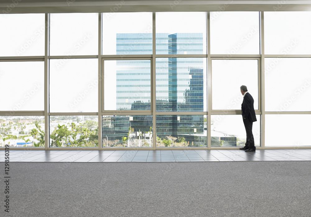 Full length of businessman looking out of office window Full length of businessman looking out of office window