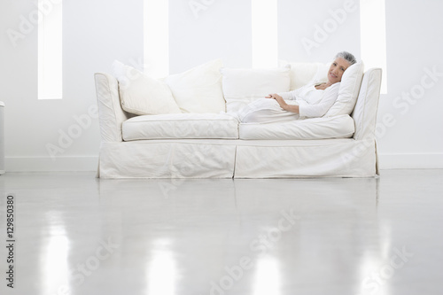 Full length portrait of senior woman sitting on sofa in spacious room