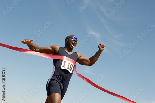 Low angle view of an African American male runner winning race against blue sky