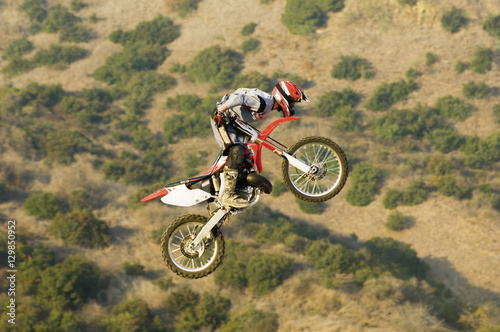 Full length of male motor bike rider on a motorcycle flying through the air with mountain in the background