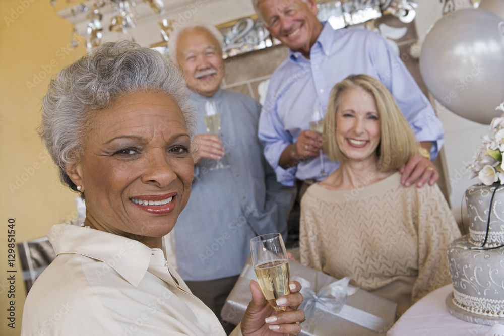 Portrait of an African American senior woman holding glass of champagne with friends in he background Portrait of an African American senior woman holding glass of champagne with friends in he background