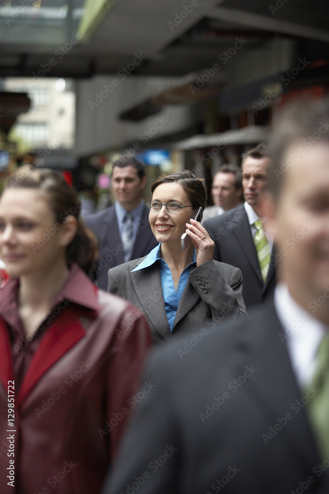 Businesswoman using mobile phone amidst coworkers while looking away Businesswoman using mobile phone amidst coworkers while looking away
