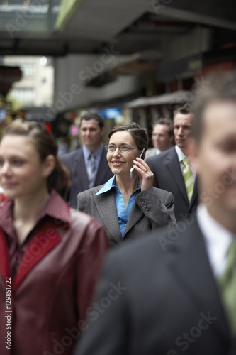 Businesswoman using mobile phone amidst coworkers while looking away