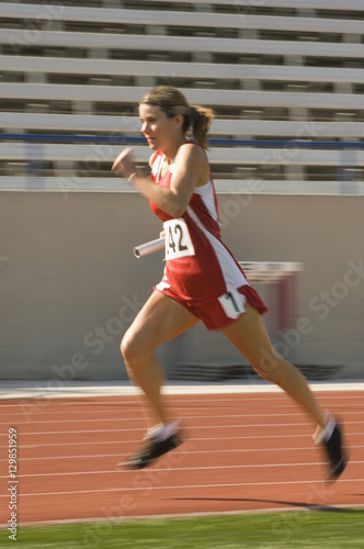 Full length of female athlete running with baton in race track