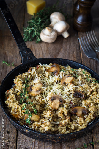Risotto with mushrooms served in iron skillet on wooden table. Close up view, rustic style