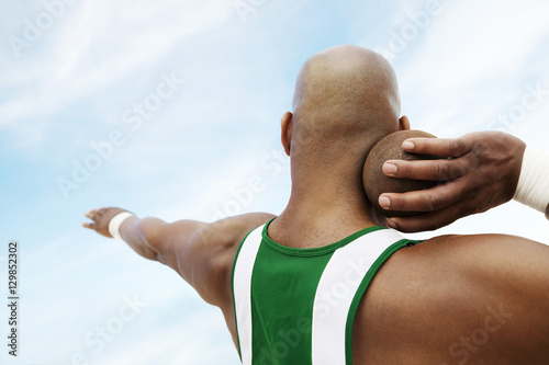 Closeup rear view of a shot putter preparing to toss shot put against the sky photo