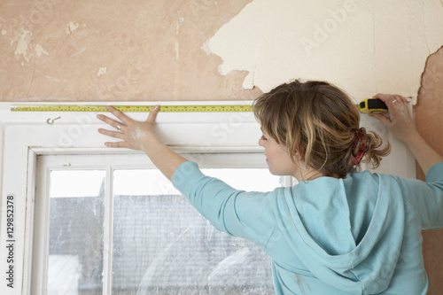 Rear view of woman measuring window frame with tape in unrenovated house photo