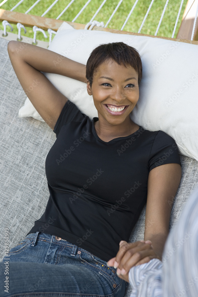 Happy African American woman holding hands on man while relaxing on hammock Happy African American woman holding hands on man while relaxing on hammock