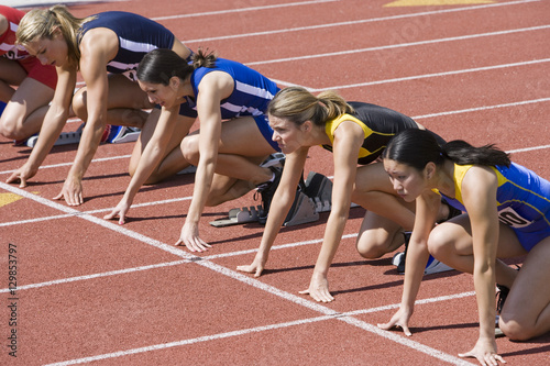 Multiracial female athletes preparing for race at starting blocks