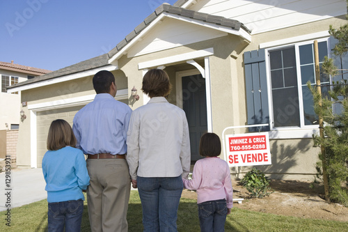 Rear view of family standing in front of house for sale