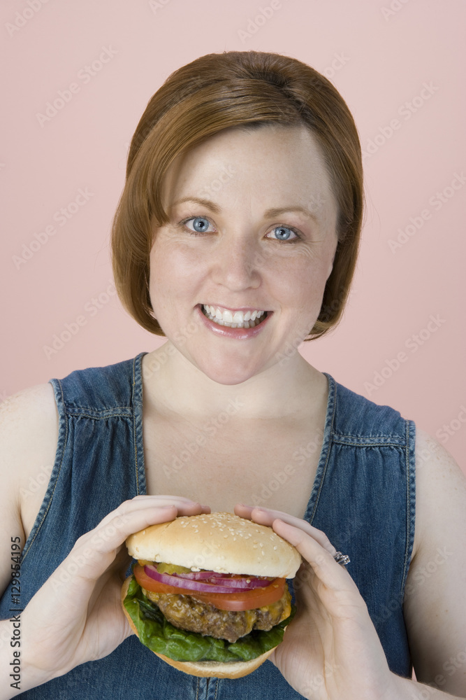 Portrait of happy middle aged woman holding hamburger over colored background