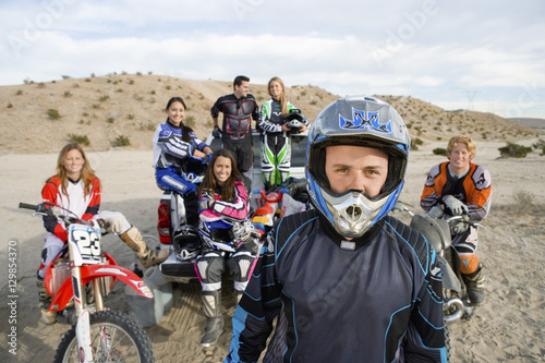Portrait of off road motor biker standing with friends in the background at track