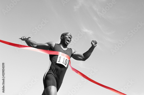 Low angle view of an African American male runner crossing finish line against blue sky