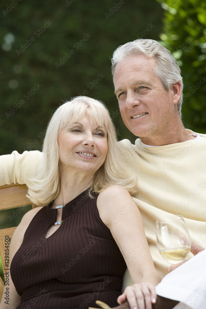 Middle aged couple relaxing on bench with wineglass outdoors
