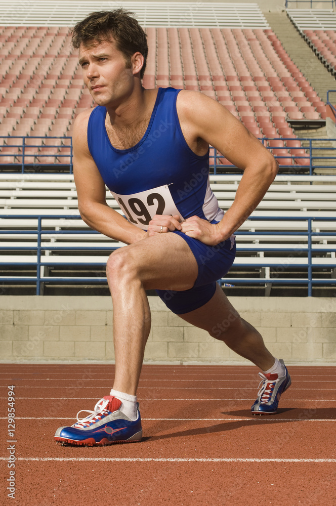 Full length of confident male athlete stretching in racing field