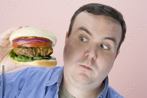 Middle aged man looking at hamburger over pink background