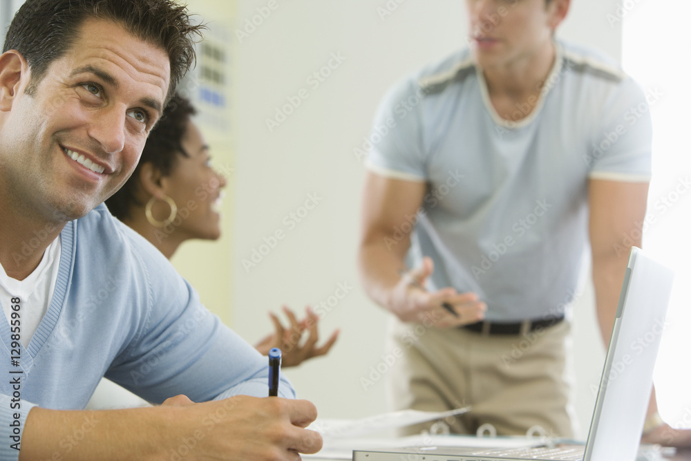 Smiling businessman with colleagues discussing in background Smiling businessman with colleagues discussing in background