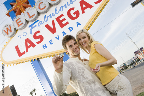 Portrait of Caucasian couple holding casino chips standing against 'Welcome To Las Vegas' sign