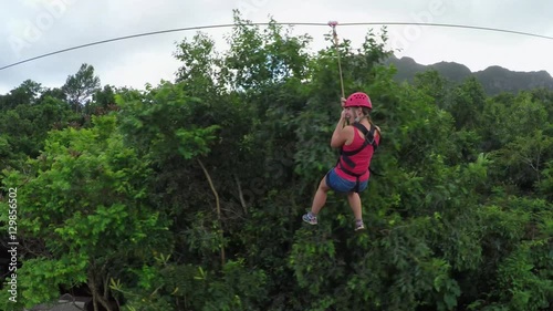 Young girl smiling and screaming when zipling on cable above lush rainforest photo