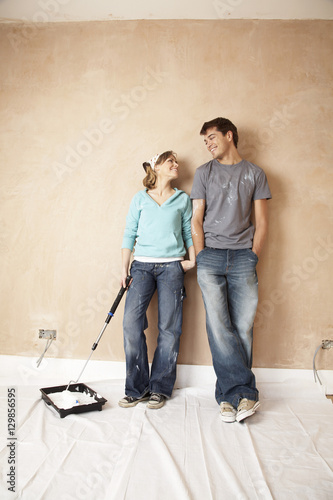 Woman dipping paint roller in paint while looking at man in unrenovated room