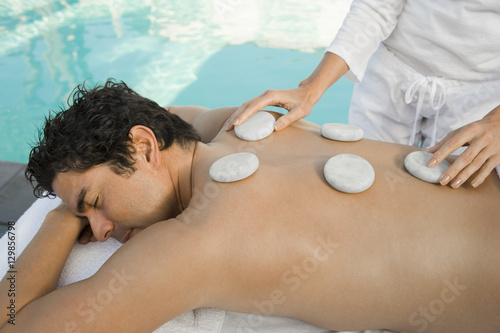 Hispanic man getting a hot stone massage by pool at a resort spa