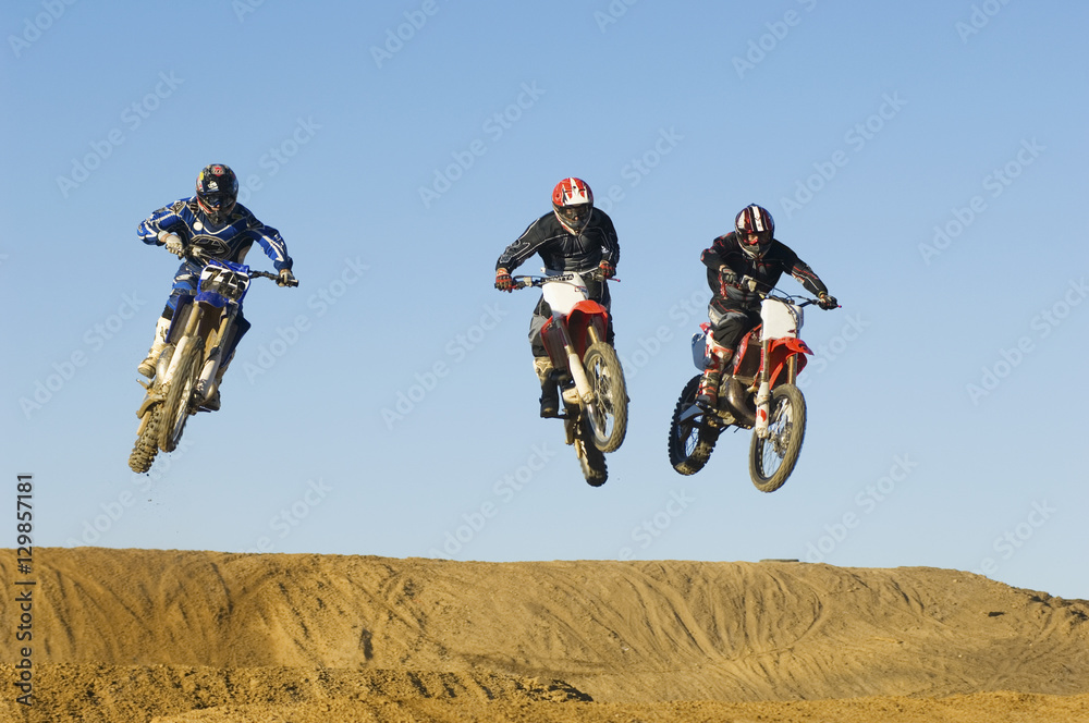Three motocross male racers racing against clear blue sky Three motocross male racers racing against clear blue sky