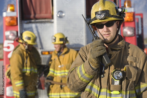 Portrait of a middle aged firefighter talking on radio with colleagues standing Fototapet