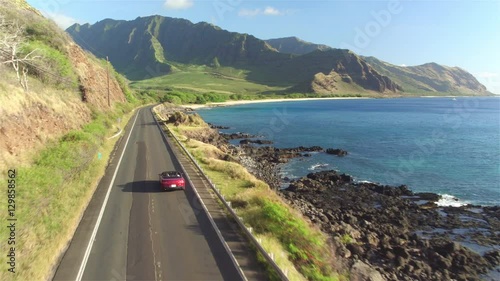 AERIAL: Couple in red convertible car driving along Hawaiian coastal road