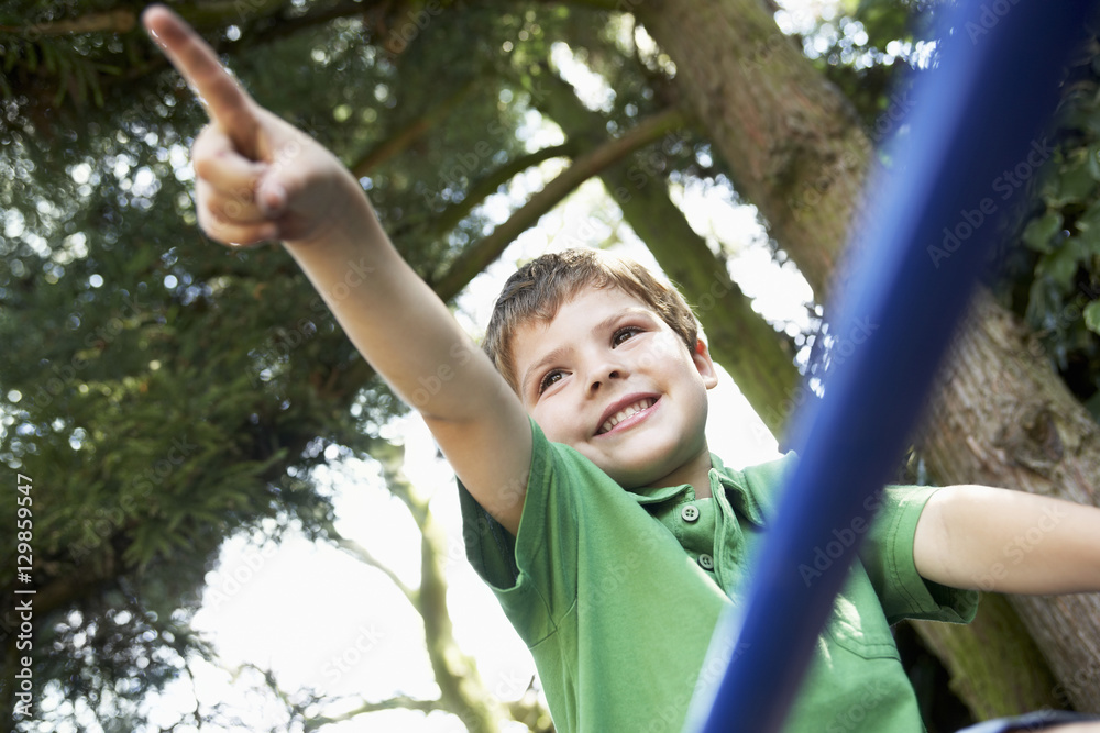 Young boy sitting on monkey bars and pointing away in the backyard