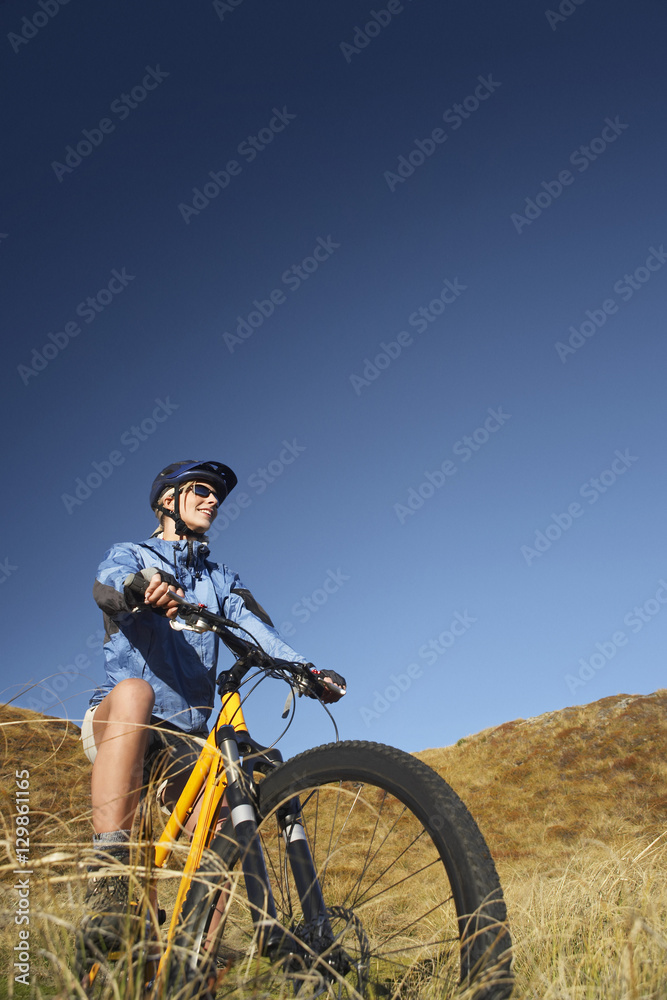 Low angle view of a young woman riding bicycle in field against clear blue sky Low angle view of a young woman riding bicycle in field against clear blue sky