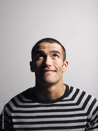 Slika na platnu Smiling young man in striped tshirt looking up against gray background