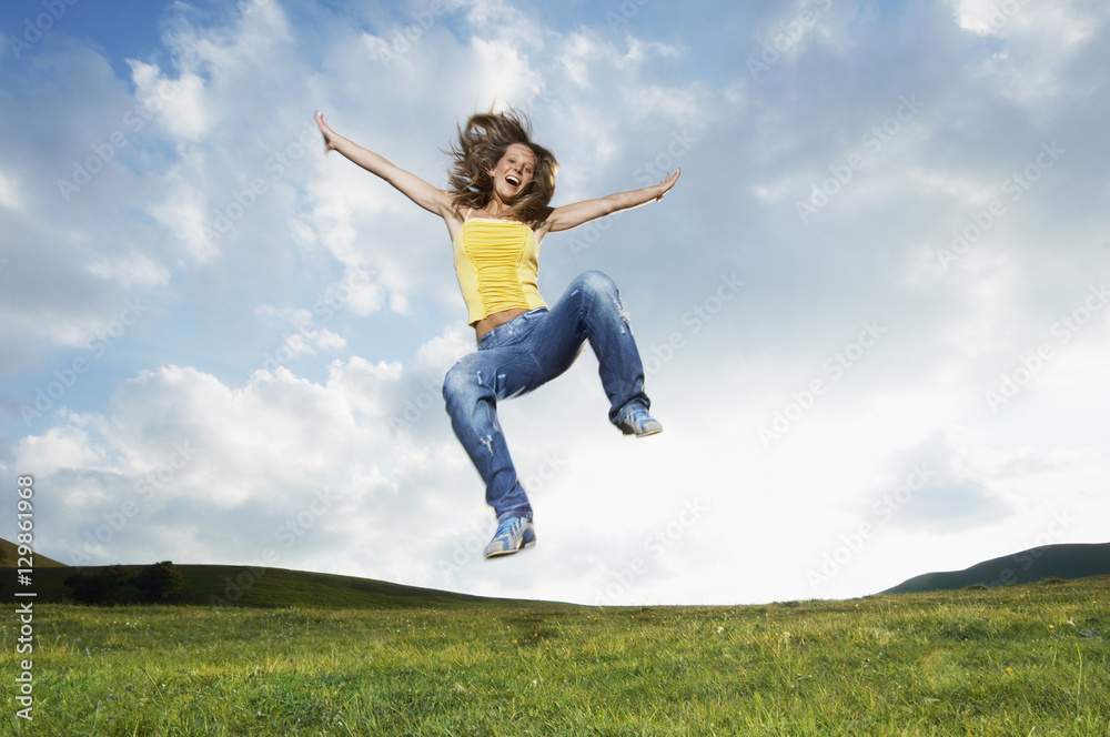 Young woman with arms outstretched screaming while jumping in park