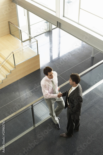High angle view of businessmen shaking hands while standing by railing in office