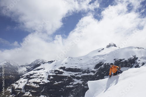 Male mountain climber sitting on snowy peak against mountains and clouds